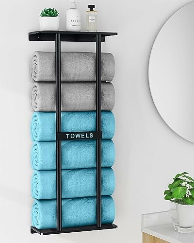 Wall-mounted towel holder with rolled gray and blue towels, shelf with plant and toiletries.